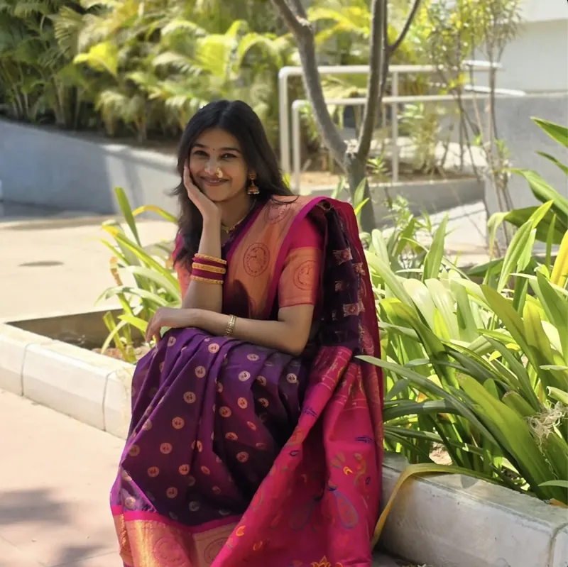 Khushi in a purple saree, sitting in a garden